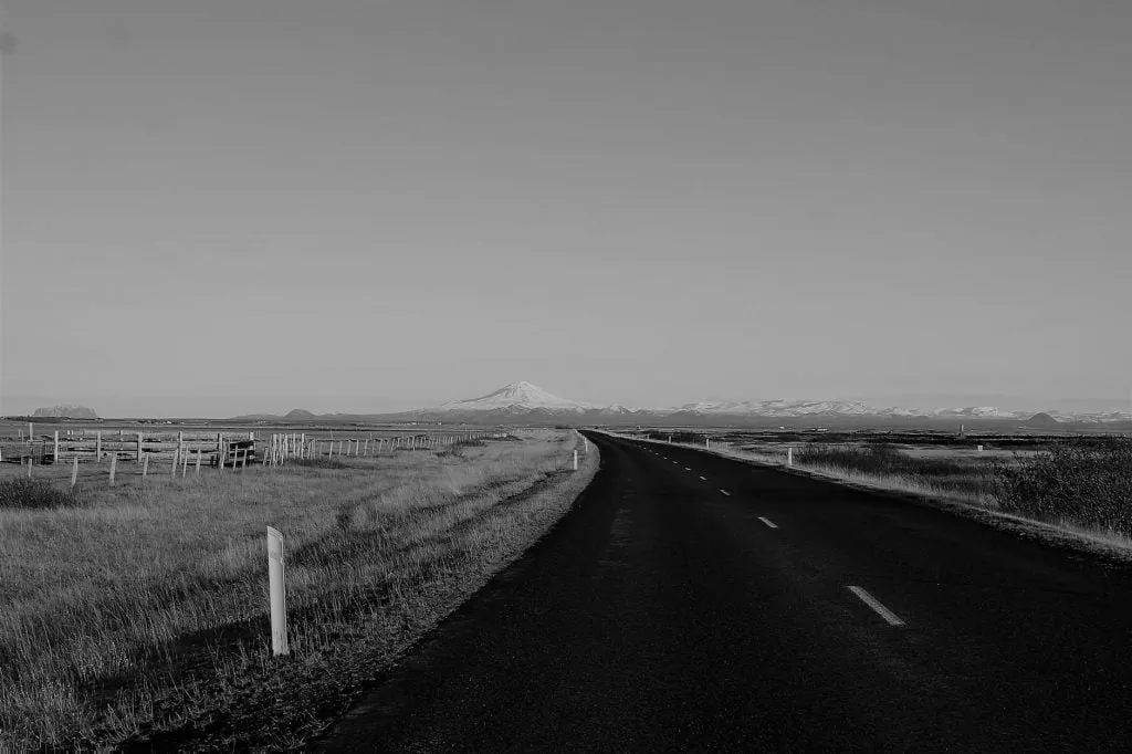 grayscale photo of road in the middle of grass field